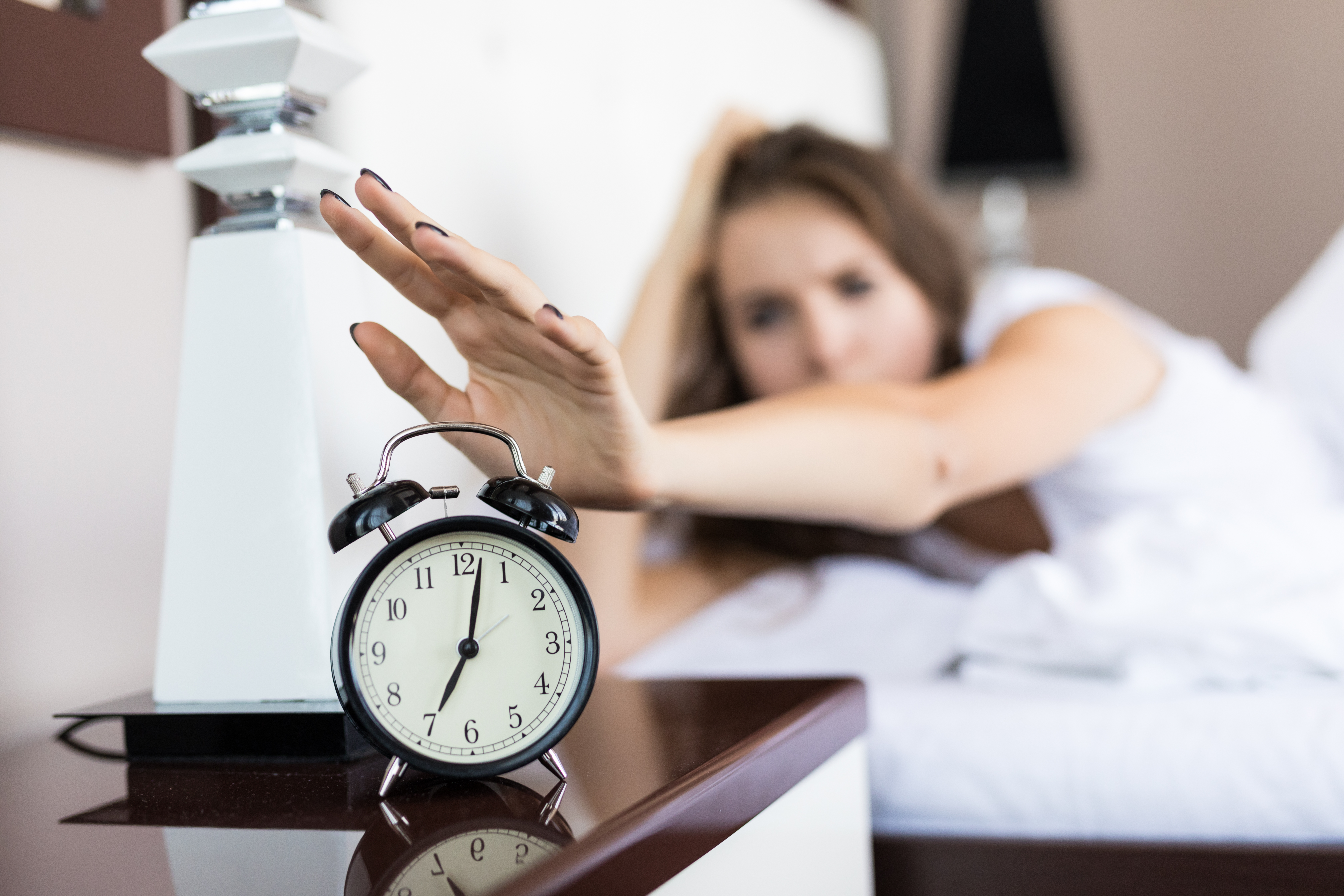 Wenn Routinen Urlaub hatten: Wie Marken Zeitfenster für Veränderung nutzen können Eine Frau liegt im Bett und streckt die Hand nach einem klingelnden Wecker auf dem Nachttisch aus, um ihn auszuschalten.