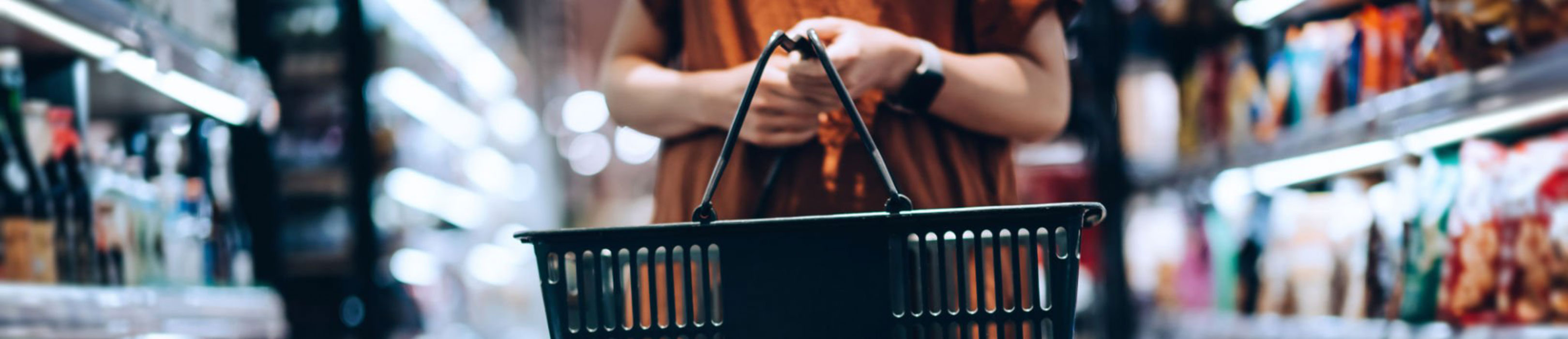 A person holding an empty shopping basket in a store, with blurred shelves in the background.